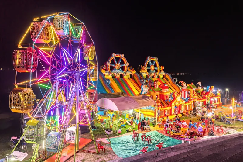 An illuminated Ferris wheel and inflatable bouncy castle light up a night funfair in Vientiane.