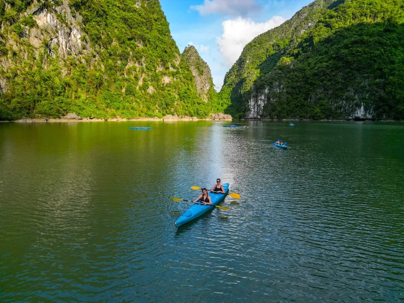Kayakers paddle through a calm lagoon between towering limestone cliffs in Lan Ha Bay.