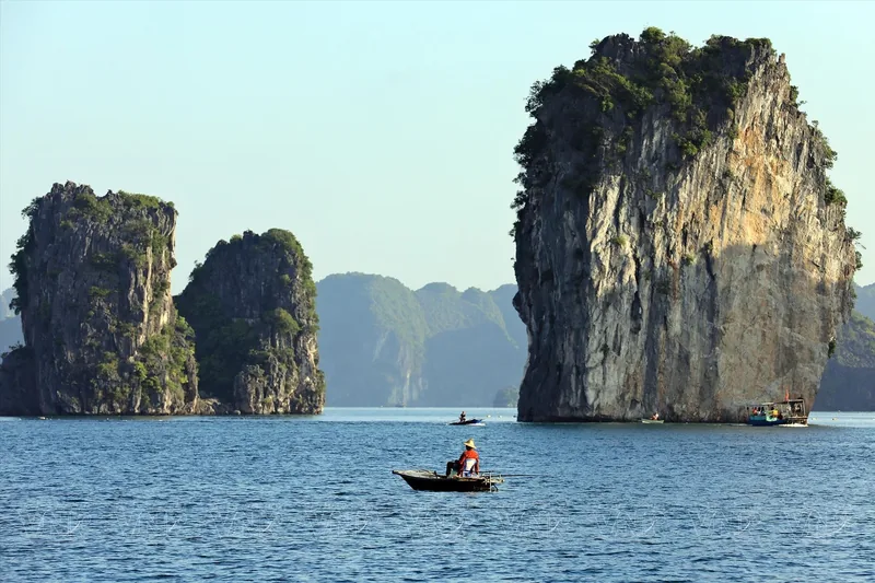 A small rowing boat glides past towering limestone karsts in Lan Ha Bay.