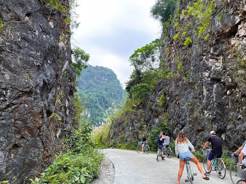 Cyclists ride through a limestone karst gorge on a paved road near Viet Hai village, Cat Ba.
