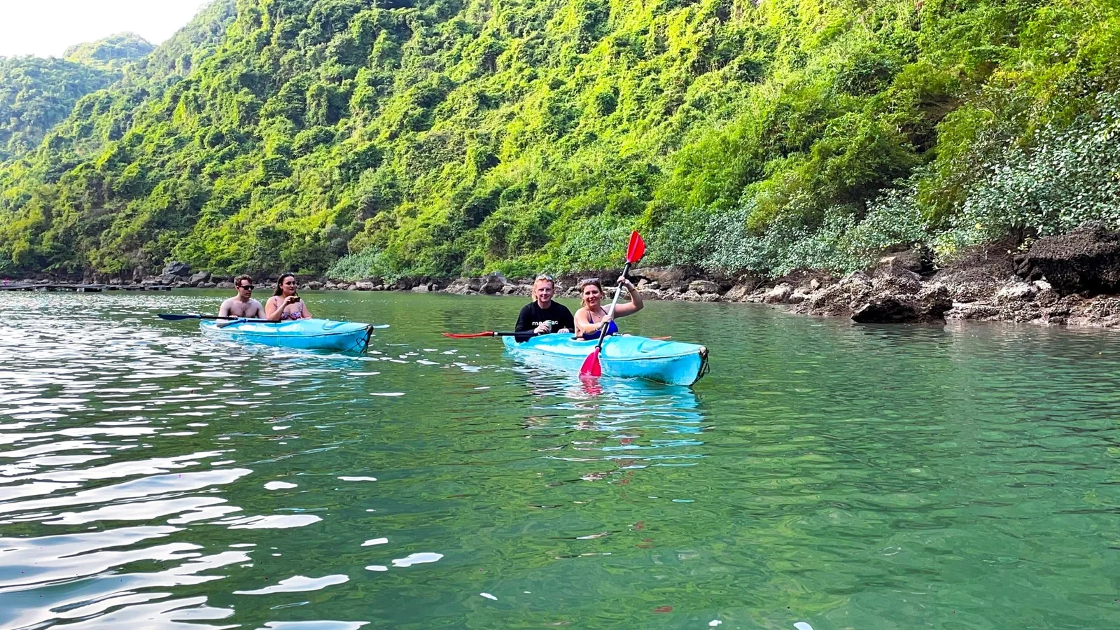 Tourists paddle blue kayaks along a limestone karst shoreline in Lan Ha Bay near Cat Ba.