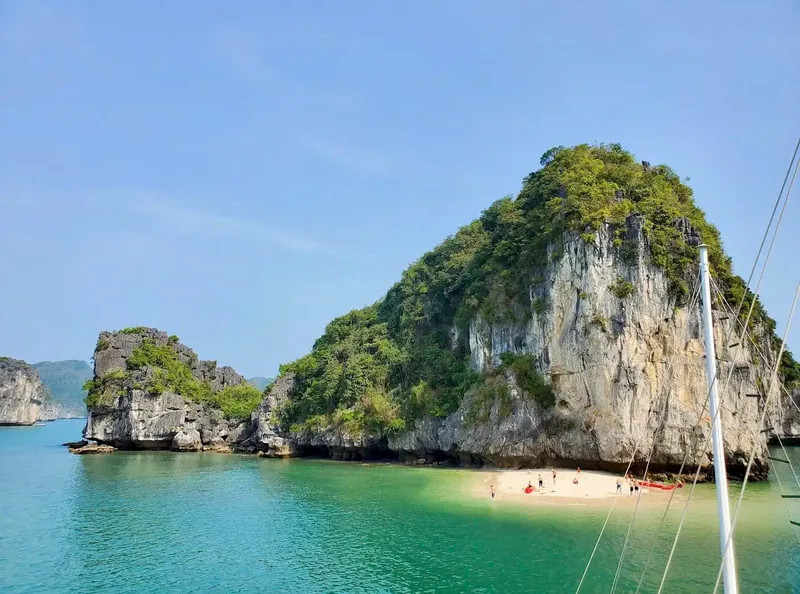 Limestone karsts rise beside a small sandy beach with turquoise water in Lan Ha Bay.