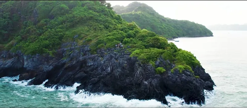 Waves crash against a green, jungle-covered rocky headland at Cat Ba island's coastline.