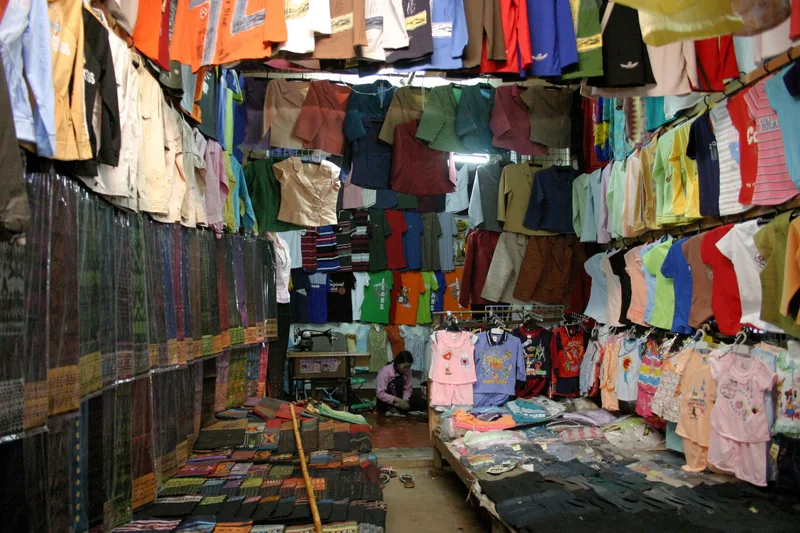 Colorful clothing hangs densely in a crowded textile stall at a market in Luang Prabang.