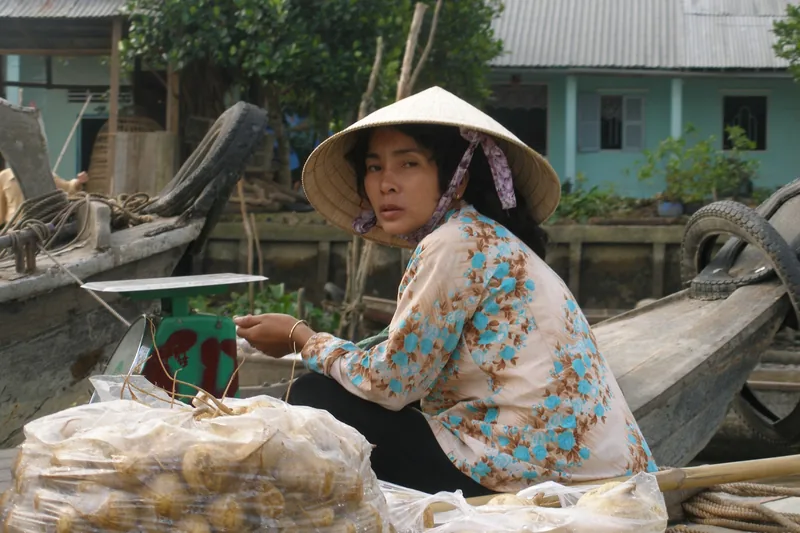 A woman in a conical hat sells goods from her boat at a floating market in the Mekong Delta.