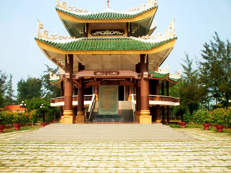 A two-tiered pavilion with green tile roofs and red columns houses a memorial stele in the Mekong Delta.