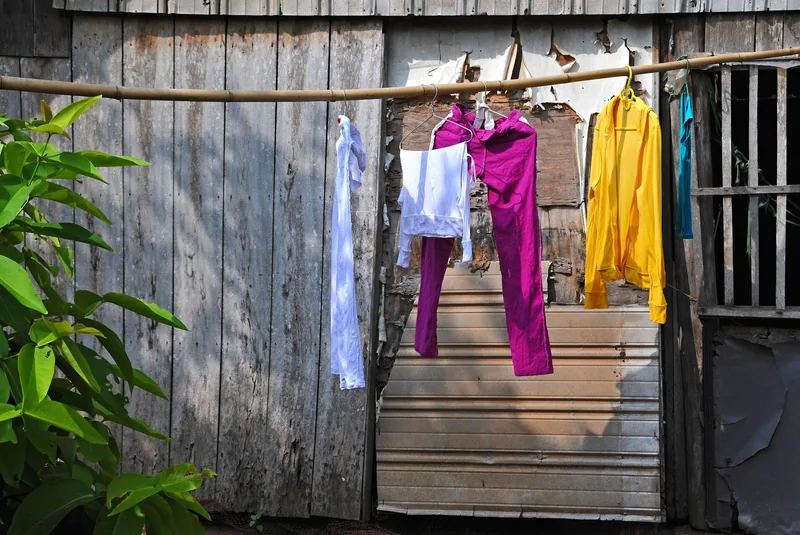 Colorful clothes hang on a bamboo pole outside a weathered wooden house in the Mekong Delta.