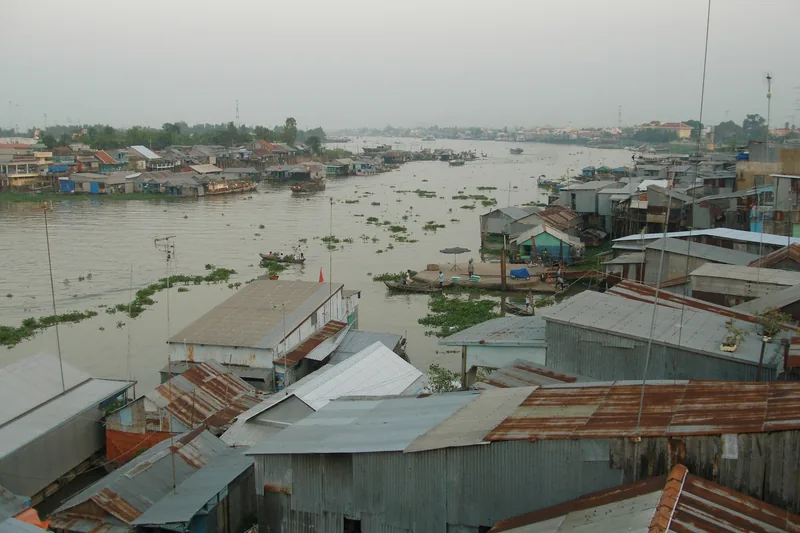 Rusty tin rooftops line the Hau River with wooden boats and floating water hyacinth in Chau Doc, Vietnam.