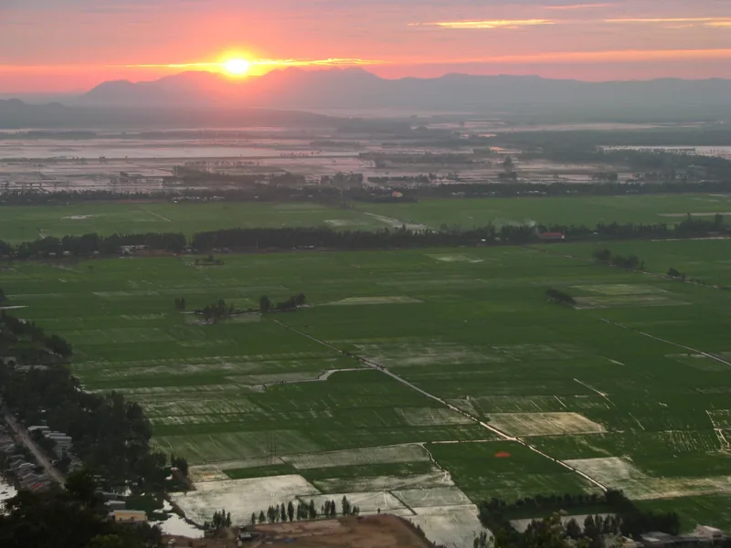 Sunset glows over a patchwork of green rice paddies stretching across the Mekong Delta.