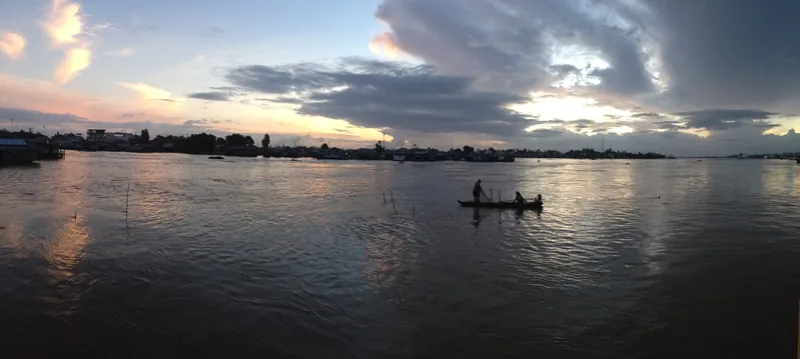 A small boat drifts on the wide river at Chau Doc under a dramatic sunset sky.