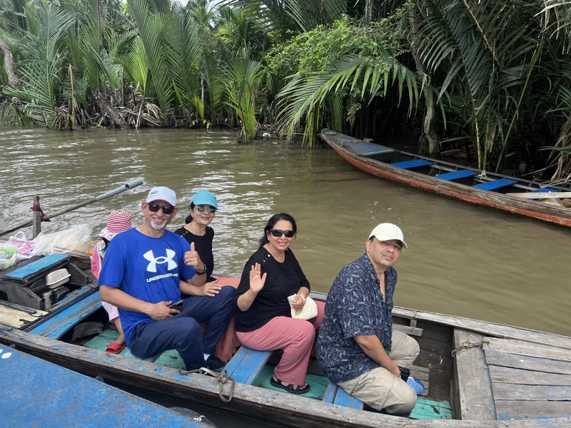 Tourists smile on a wooden boat cruising a palm-lined canal in the Mekong Delta.