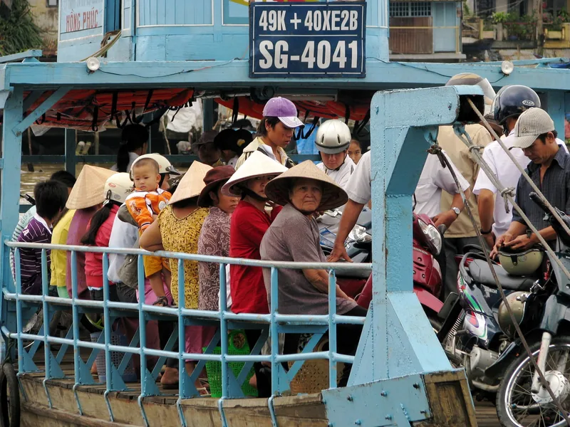 Passengers with conical hats and motorbikes crowd a blue ferry boat in the Mekong Delta.