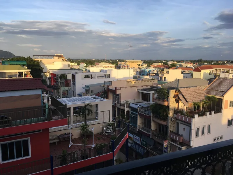 Rooftop view over the low-rise houses and rooftop terraces of Chau Doc at dusk, with a distant hill on the horizon.