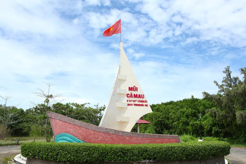 The boat-shaped monument marking Mui Ca Mau, Vietnam's southernmost point, stands under a blue sky with the national flag.