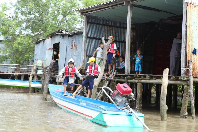 Children in life jackets board a wooden boat beside stilt houses at Mui Ca Mau, Vietnam