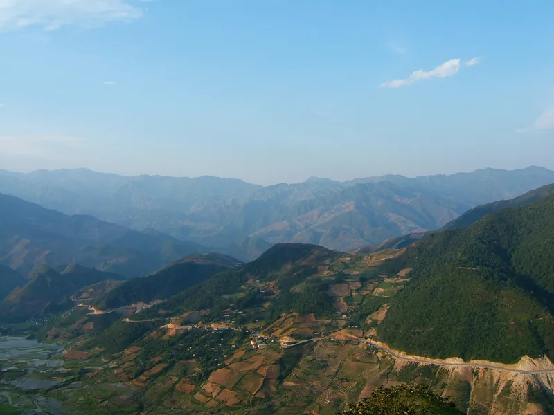 A winding mountain road cuts through terraced valleys and misty peaks near Khau Pha Pass in Mu Cang Chai.