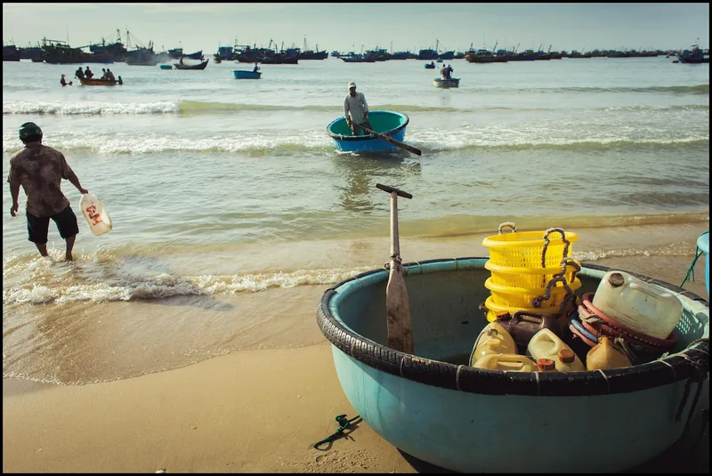 Round basket boats and fishermen crowd the shore at Mui Ne's fishing village with a fleet anchored offshore.