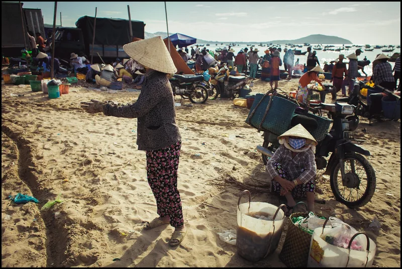 A busy morning fish market on the sandy beach at Mui Ne, with vendors in conical hats, motorbikes and baskets of catch.