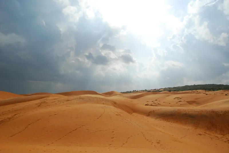 Sunlight breaks through dramatic clouds over the red sand dunes of Mui Ne, Vietnam.