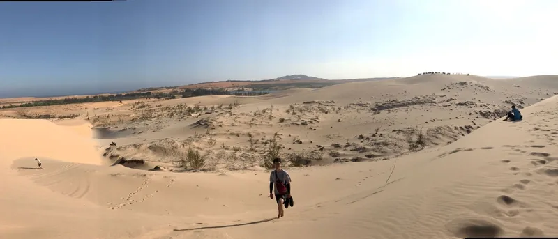 A visitor walks barefoot across the vast white sand dunes of Mui Ne under a clear blue sky.