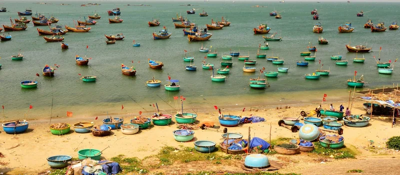 Round basket boats and wooden fishing boats crowd the shore and turquoise water at Mui Ne fishing village.
