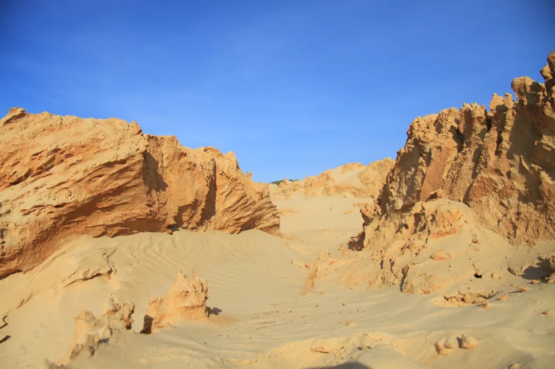 Wind-eroded orange sand dunes and rock formations under a clear blue sky in Binh Thuan.