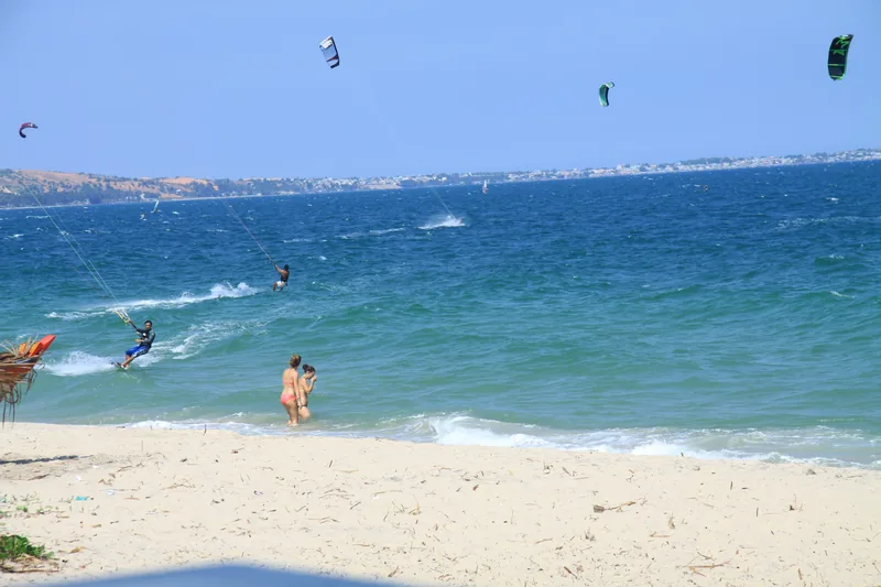 Kitesurfers glide across turquoise waves off a sandy beach in Binh Thuan.