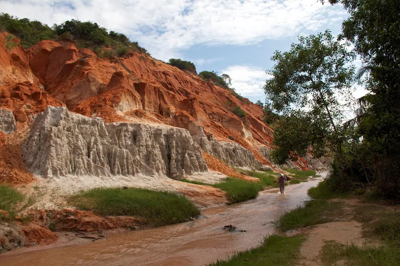 A person walks along the shallow stream beneath red and white eroded canyon walls at Fairy Stream in Mui Ne.