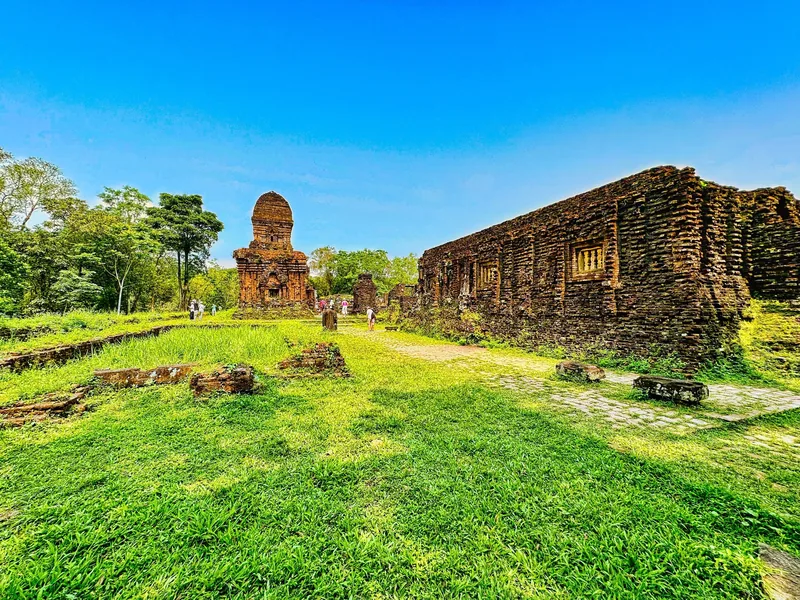 Ancient brick towers and ruined walls stand amid green grass at the My Son Cham temple complex in Vietnam.