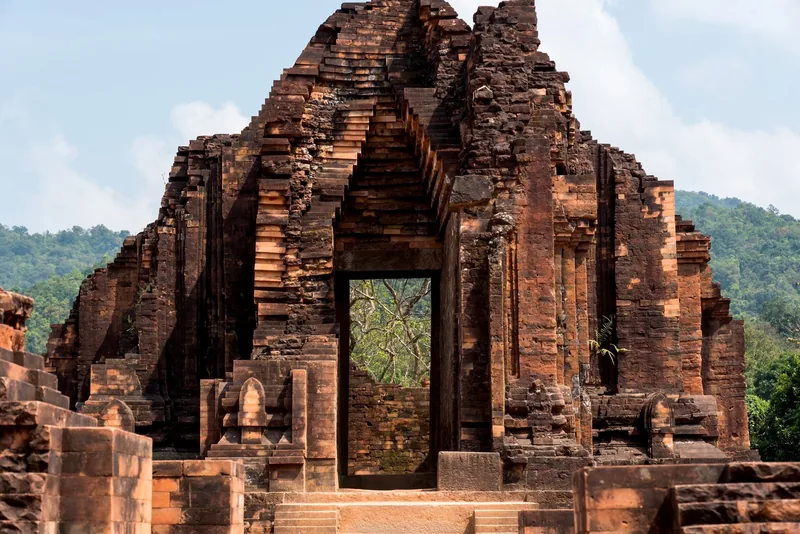 Ancient brick tower ruins with an archway doorway stand at My Son Sanctuary in Vietnam.