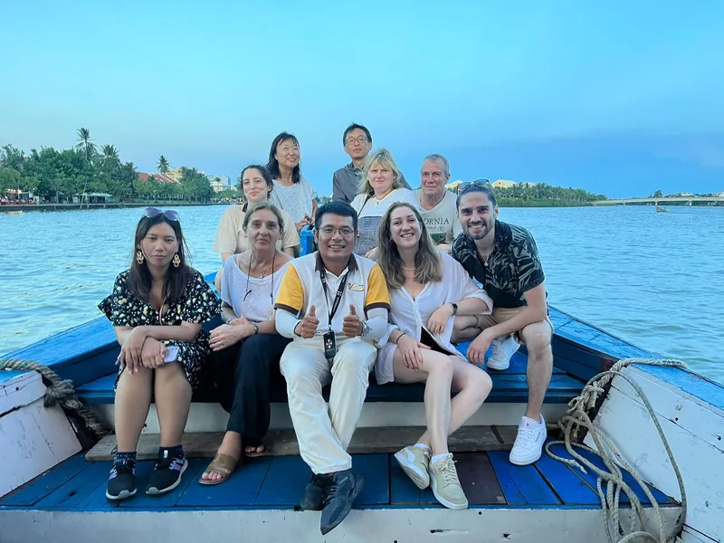 A group of tourists smiles together on a traditional wooden boat on the river near Hoi An.