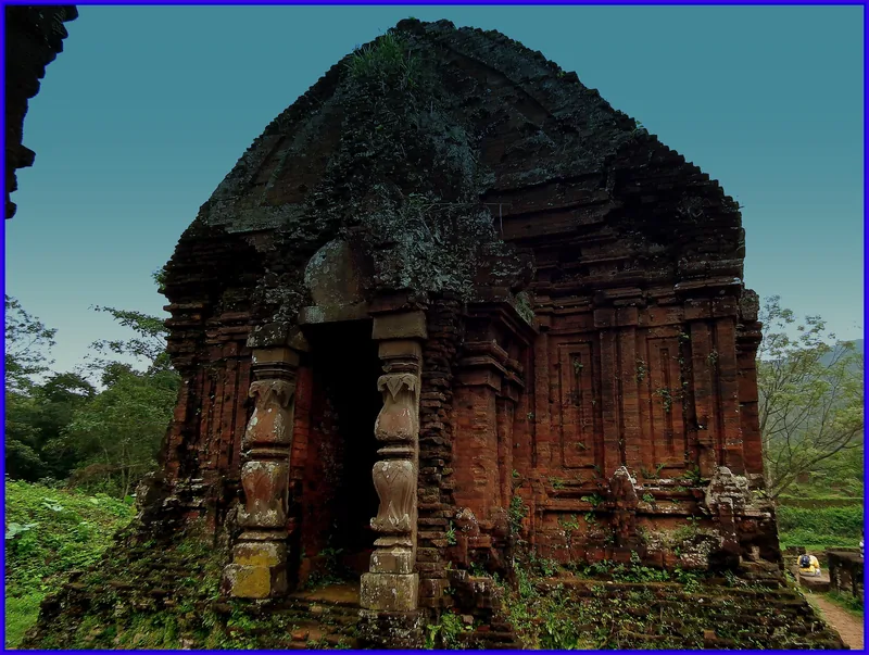 Ancient brick Cham tower with carved stone doorway stands amid greenery at My Son sanctuary, Vietnam.