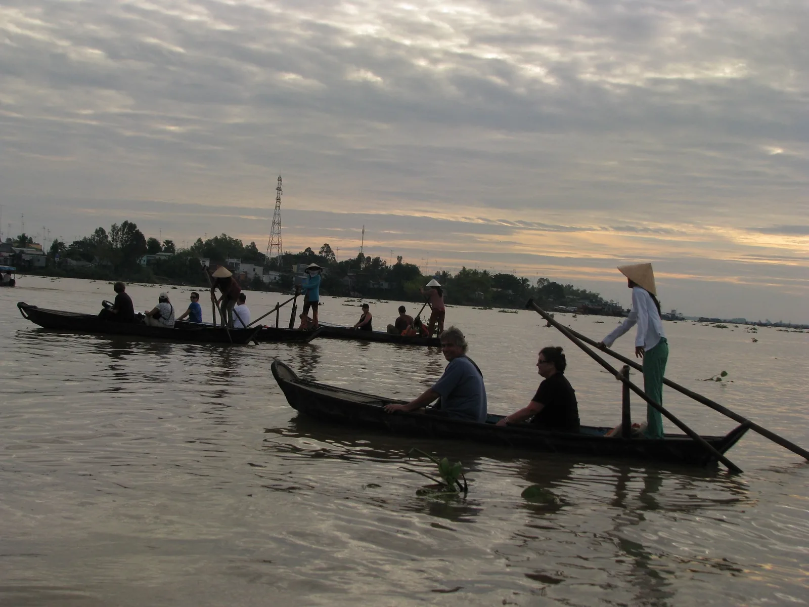 Tourists ride small wooden boats rowed by local boatmen on the Mekong River at dusk.