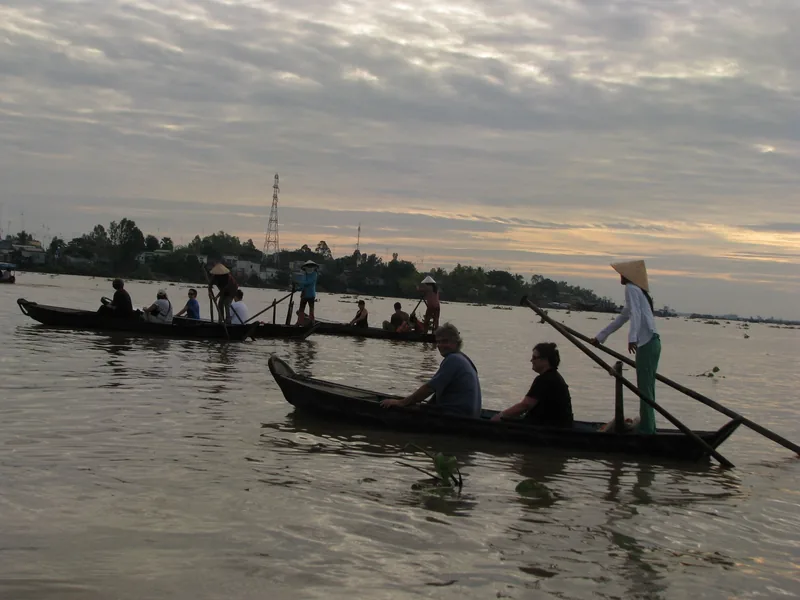 Tourists ride small wooden boats rowed by local boatmen on the Mekong River at dusk.