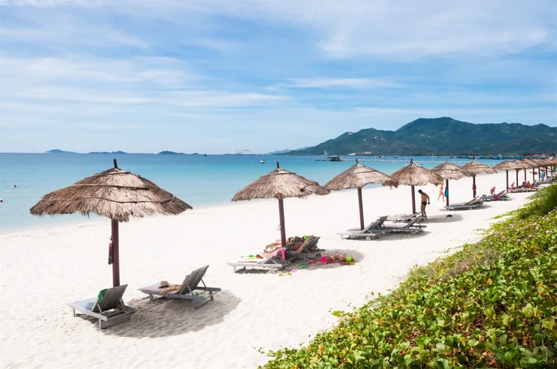 Thatched umbrellas and sun loungers line the white sand of Doc Let beach in Nha Trang under a bright sky.