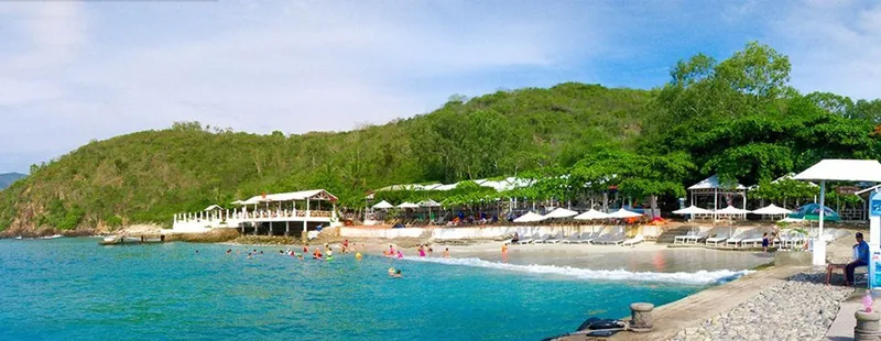 A curved sandy beach with lounge chairs and swimmers backs onto a forested hill near Nha Trang.