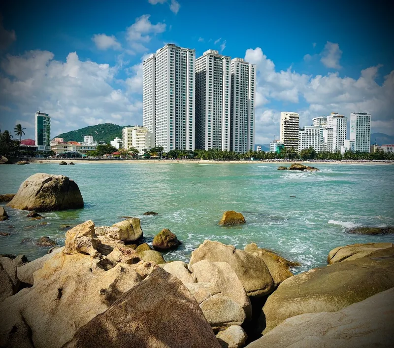 High-rise towers line the beachfront of Nha Trang, seen past rocky boulders and turquoise sea.