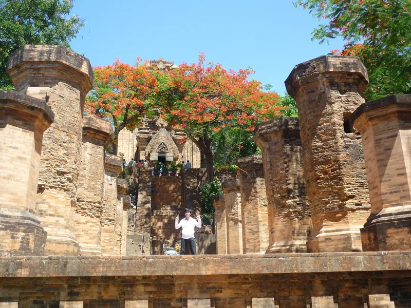 Ancient brick pillars and stairways lead up to Po Nagar Cham towers under a flowering flamboyant tree in Nha Trang.