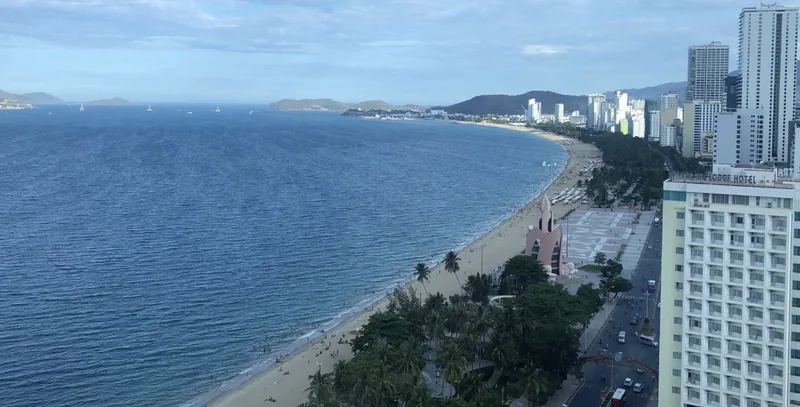 Aerial view of Nha Trang's curved coastline with sandy beach, palm trees and high-rise hotels along the bay.