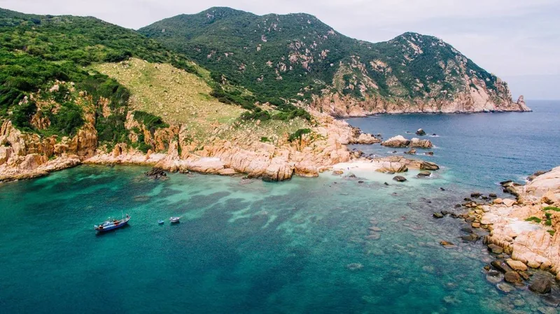 Turquoise waters and rocky green hills surround a small fishing boat near Nha Trang's coast.