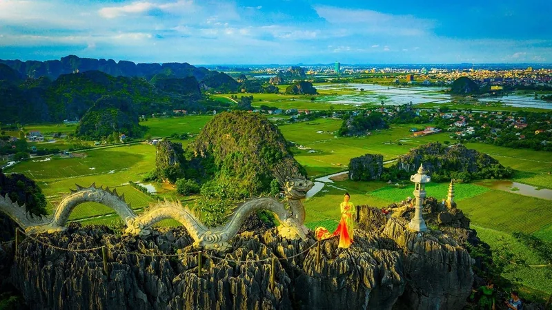 A woman in a red dress stands beside a dragon sculpture atop Hang Mua viewpoint overlooking Ninh Binh's limestone karsts.