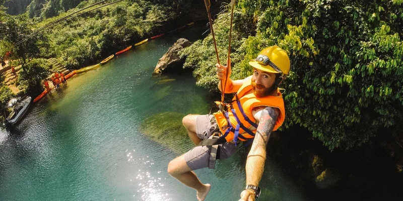 A tourist wearing a helmet and life jacket zip-lines over a turquoise river near Dark Cave in Quang Binh.