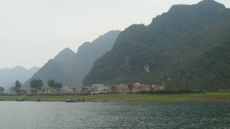 Small boats float on a river beside a riverside village beneath limestone karst mountains in Phong Nha.