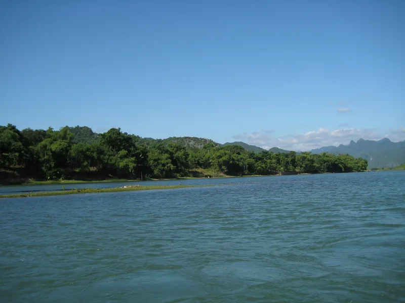 A wide river flows past forested hills under a clear blue sky near Phong Nha.