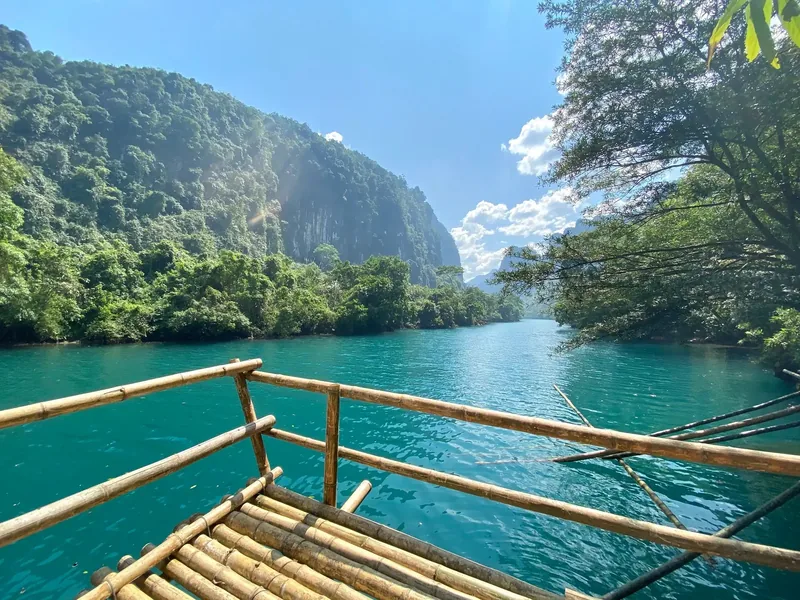 A bamboo raft glides across turquoise water surrounded by limestone cliffs near Dark Cave, Quang Binh.