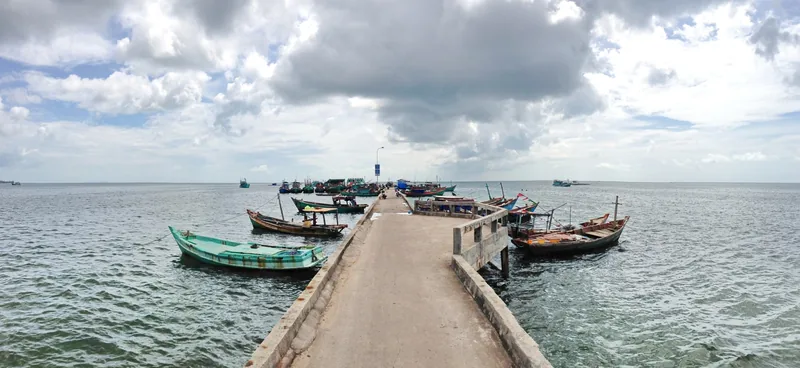 A long concrete pier stretches into the sea with fishing boats moored on both sides near Ham Ninh, Phu Quoc.