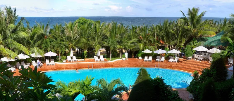 A resort swimming pool surrounded by palm trees and loungers overlooks the sea in Phu Quoc.