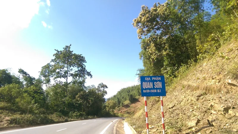 A blue road sign marks the Quan Son district boundary along a mountain highway near Pu Luong.