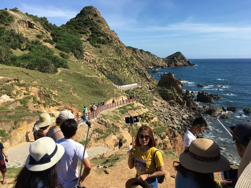 Tourists walk along a fenced coastal path beneath rocky cliffs at Eo Gio near Quy Nhon.