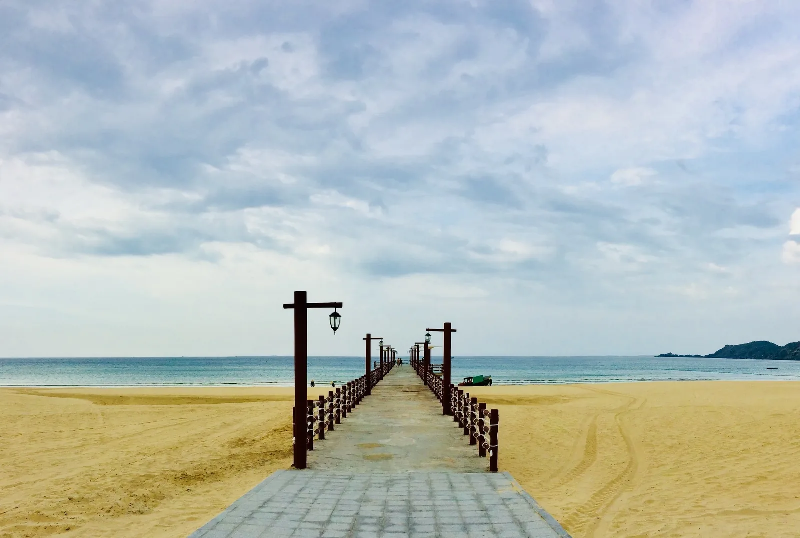 A long pier with lamp posts stretches across a sandy beach toward the sea in Quy Nhon.